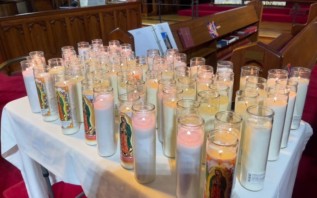 A church altar with numerous lit candles featuring religious imagery, surrounded by wooden pews, creates a serene, spiritual atmosphere.