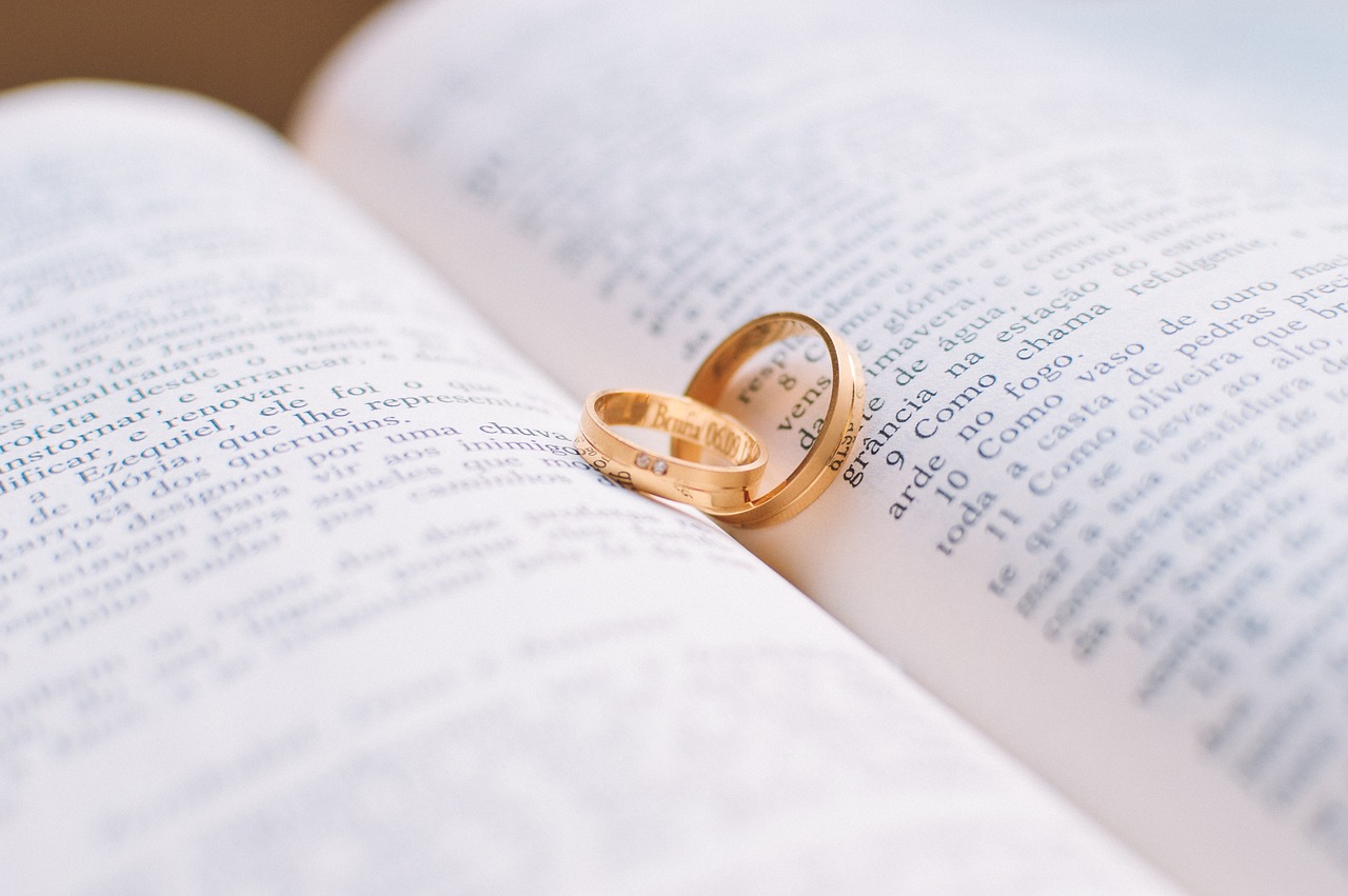 Two gold rings rest on an open book with text in Portuguese, symbolizing love intertwined with literature and commitment.